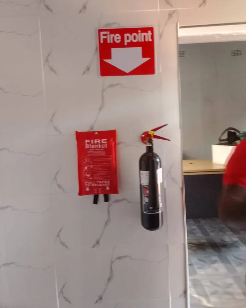 A fire blanket and extinguisher mounted under a Fire point sign on a tiled wall