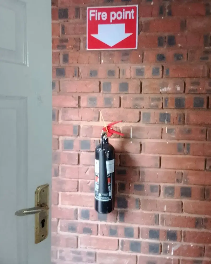 A CO2 extinguisher mounted below a red Fire point sign on a brick wall