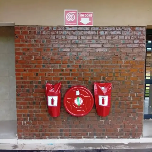 A hose reel mounted between two extinguishers in red covers at a fire point